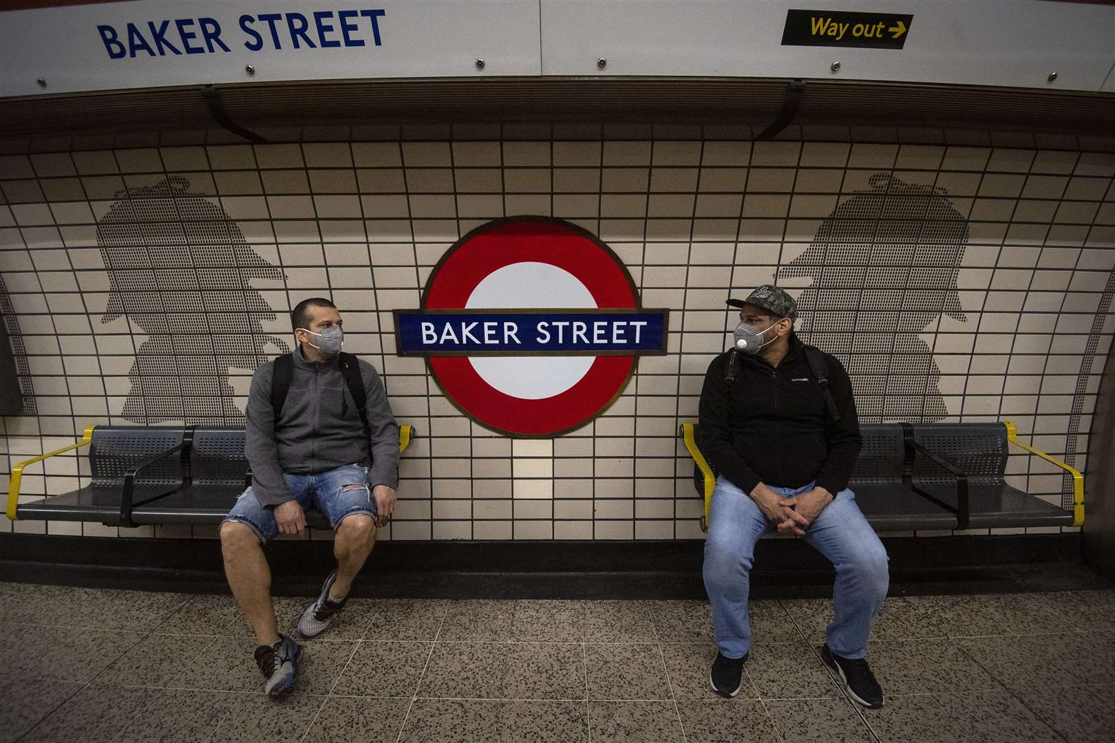 Two men in face masks sit in front of Sherlock Holmes artwork in Baker Street Tube station (Victoria Jones/PA)