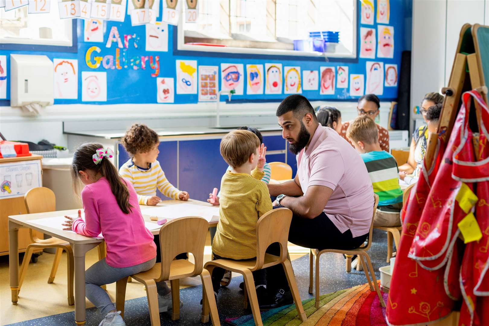 Primary school students sitting in an art classroom being taught by a teacher - stock image.