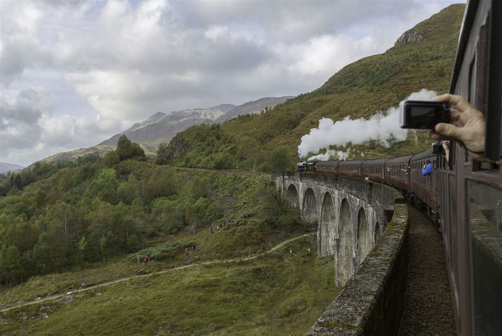 Passengers filming on their phones and cameras out of the window of the Jacobite Steam Train as it makes its way along the Glenfinnan Viaduct (Yui Mok/PA)