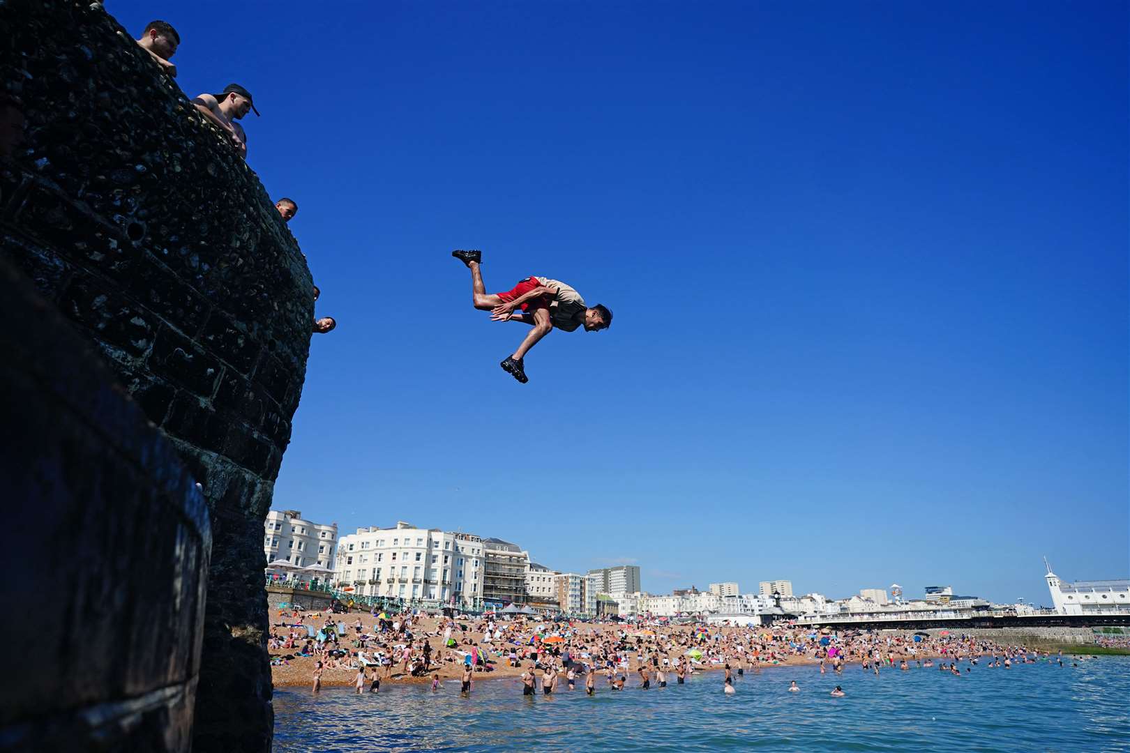 People jump into the sea from a groyne at Brighton beach in East Sussex (Victoria Jones, PA)