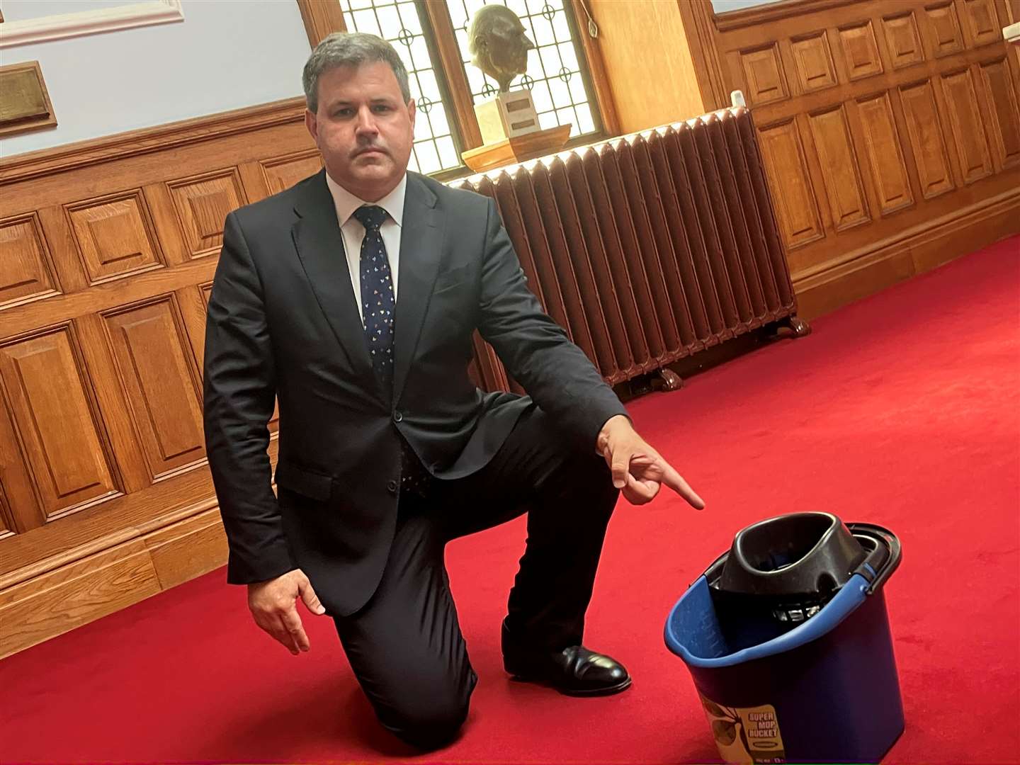 Lib Dem leader Cllr Antony Hook pointing to a bucket collecting water from the leaking roof at County Hall in Maidstone