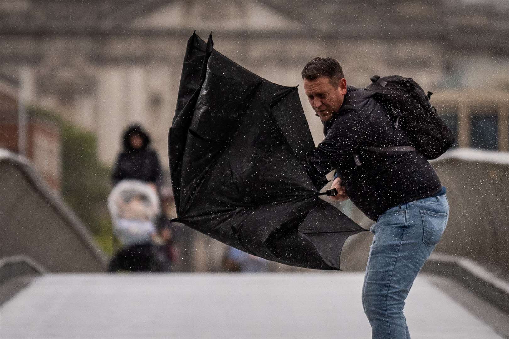 A man struggling with his umbrella on Millennium Bridge in London (Aaron Chown/PA)